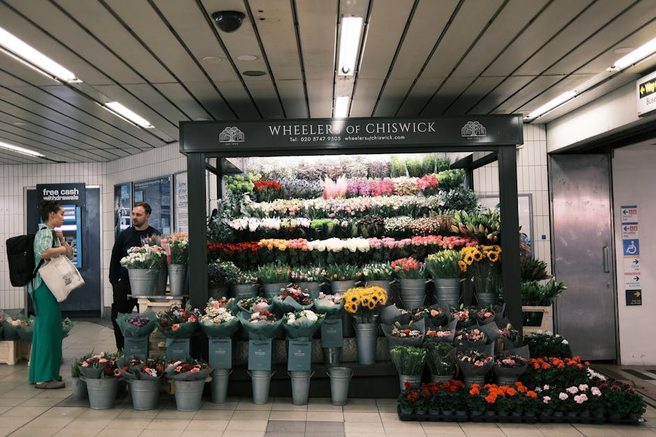 A vibrant display of fresh floral arrangements located at Wheeler of Chiswick in an underground station, featuring a variety of flowers including pink roses, white lilies, yellow sunflowers, and red g